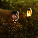 Two solar flame torch lights glowing in a garden border at dusk