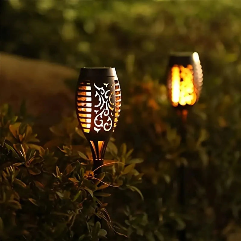 Two solar flame torch lights glowing in a garden border at dusk