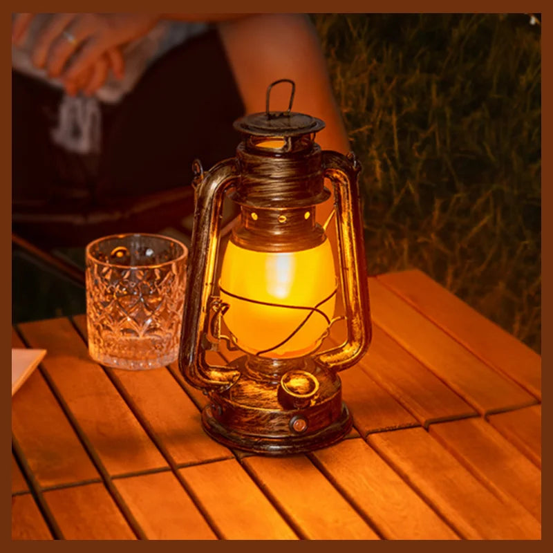 Vintage-style flame lantern lit on a wooden outdoor table beside a cut-glass tumbler