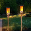 Two bamboo solar torch lights glowing in a garden at dusk