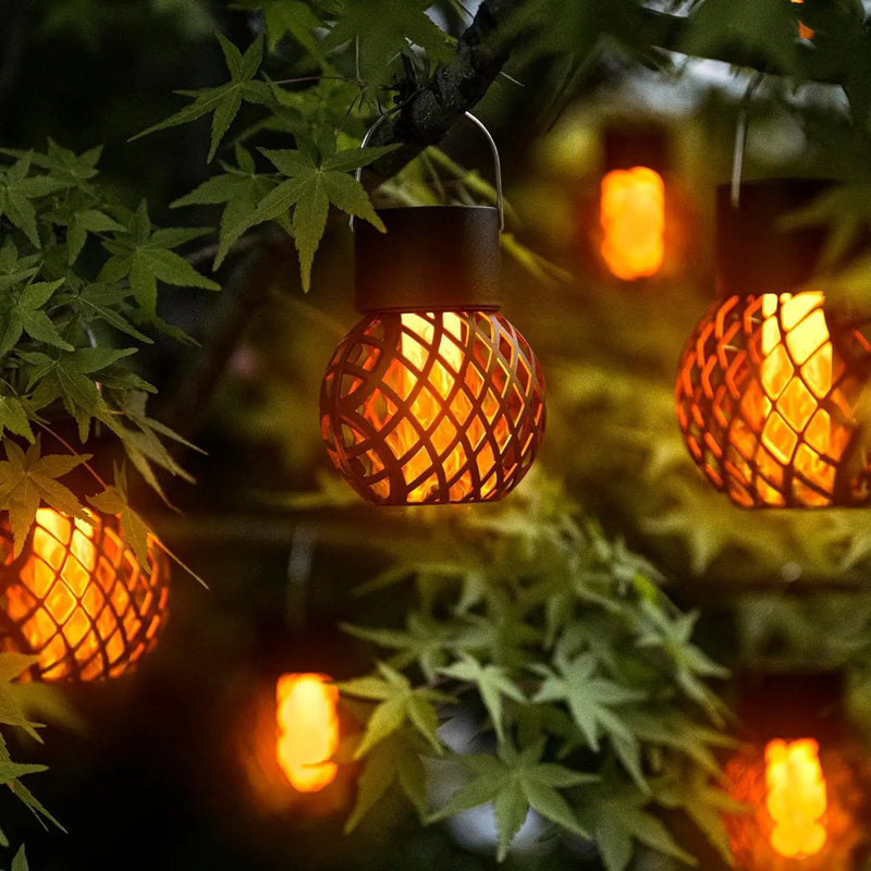 Solar flame pendant lanterns hanging among the leaves of a garden tree