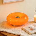 Donut LED table lamp lit on a bedside table with a reed diffuser