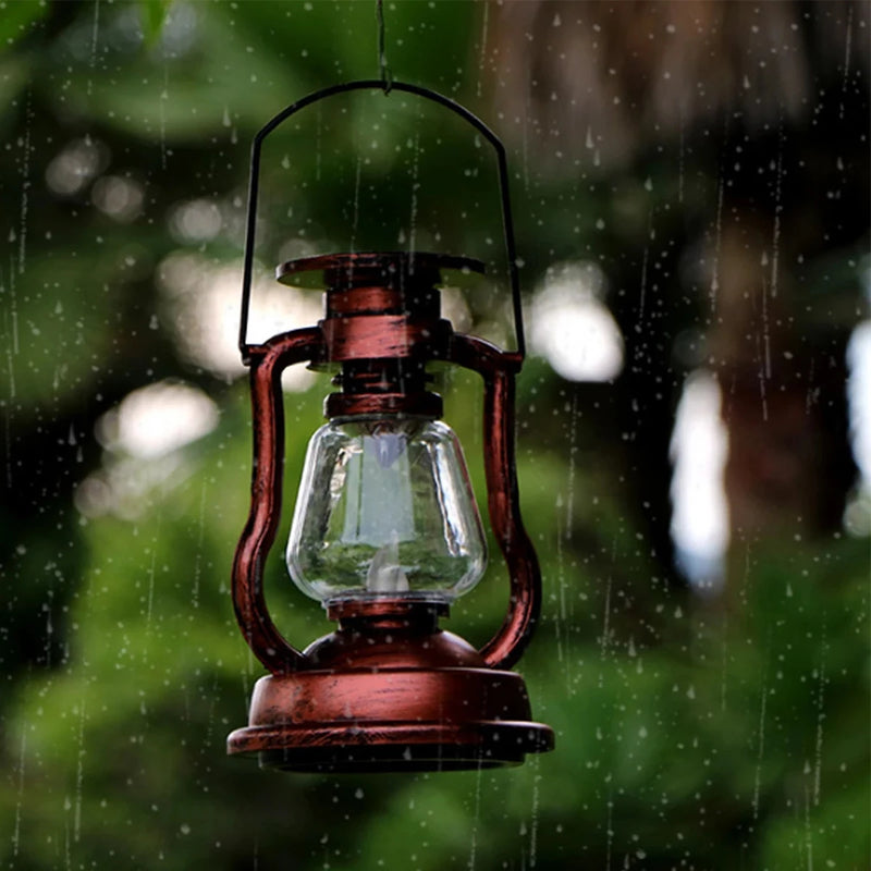 Vintage-style solar lantern hanging outdoors in the rain among green foliage