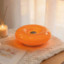 Donut LED table lamp glowing warm amber on a knitted throw beside a book