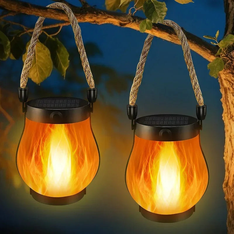 Two flame-effect lanterns with rope handles hanging from a branch at dusk
