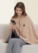 Woman on a sofa using her phone with the apricot heated shawl blanket draped over her shoulders and lap